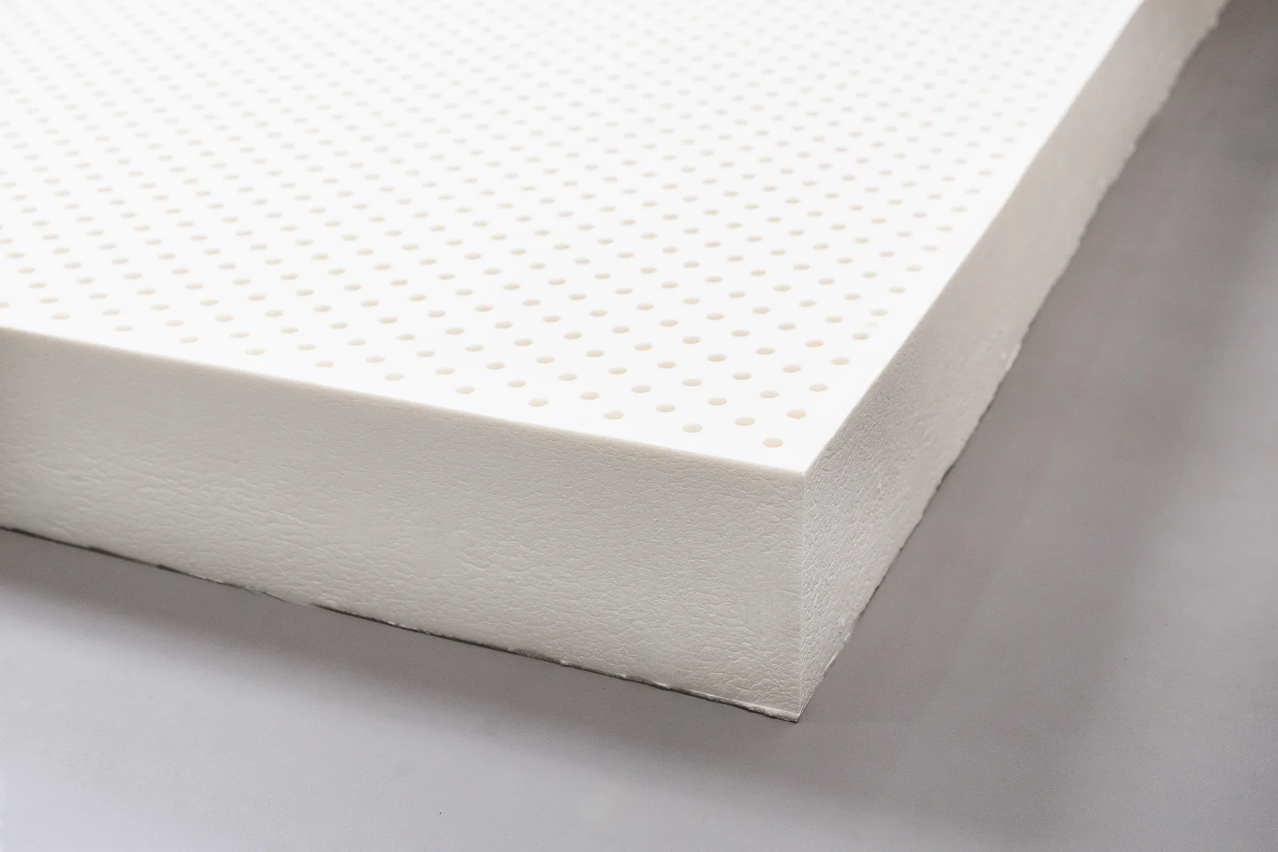 Close-up corner of a thick natural latex slab showing its perforated surface
