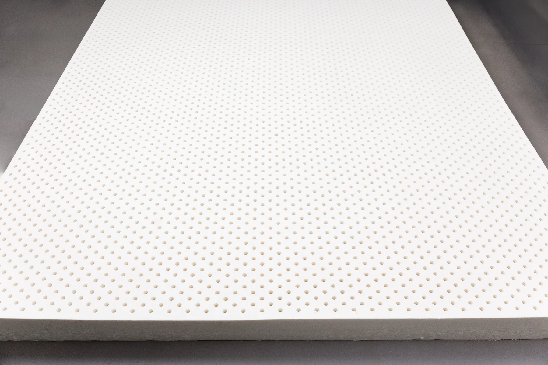 Natural latex mattress topper shown at an angle with visible perforation holes